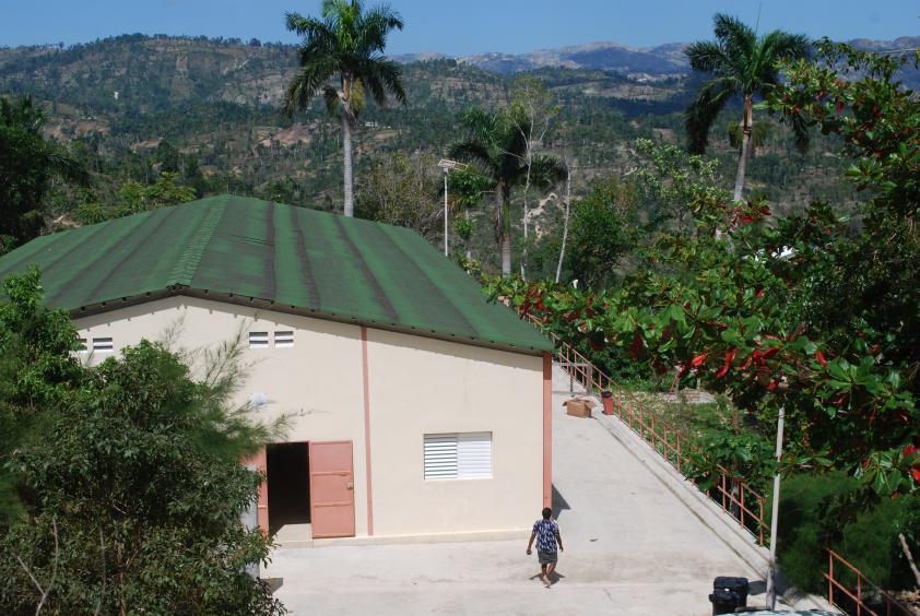 Aerial view of Villa Clinic, a clean rectangular concrete building high in the mountains, with palm trees behind.