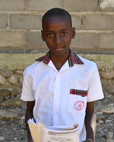 A 10-year-old boy in white shirt holds a school workbook. He has a slight smile on his face.