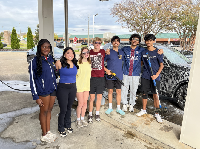 Students pose in front of a partially-washed car during their fundraiser.