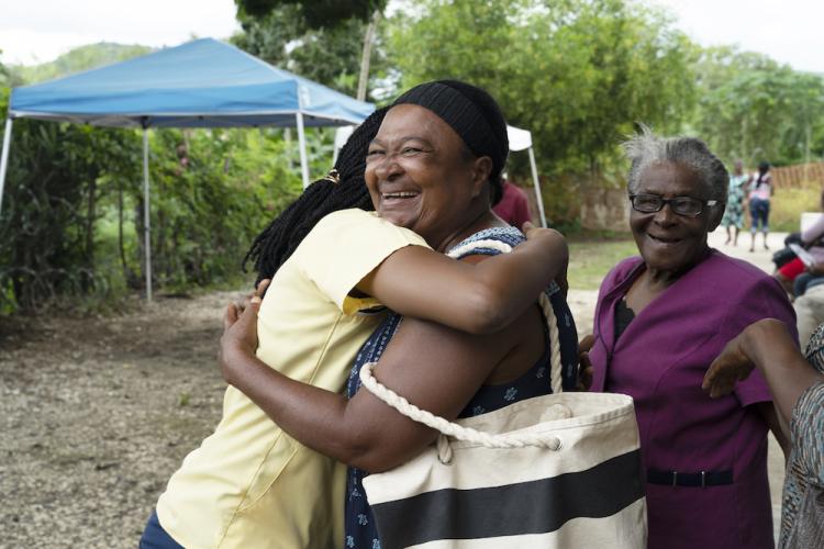 A Haitian nurse wearing pale yellow scrubs hugs a patient during an event for diabetic patents.