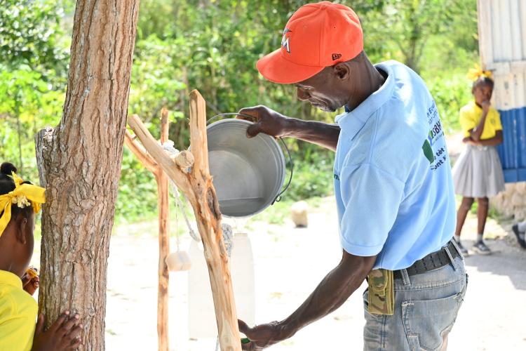 A Kore Sante/IHSD team member fills a tippy tap with fresh water.