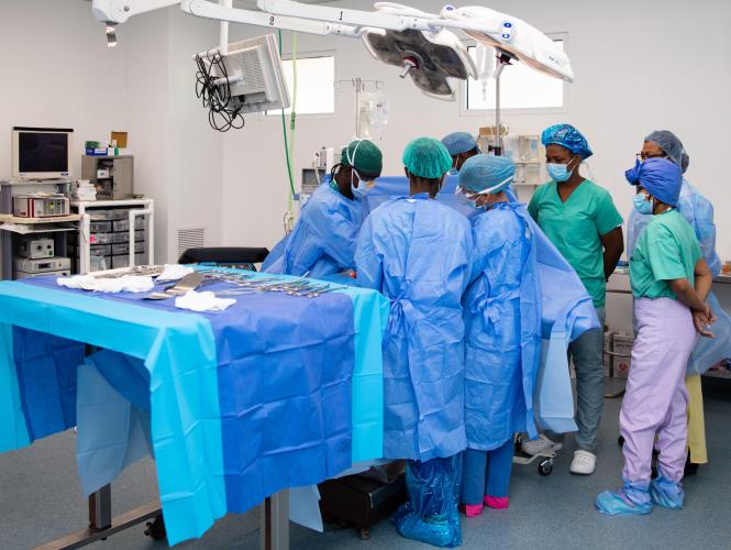View of an operating room with a half-dozen Haitian women and men, in full PPE, gathered around an unseen patient.