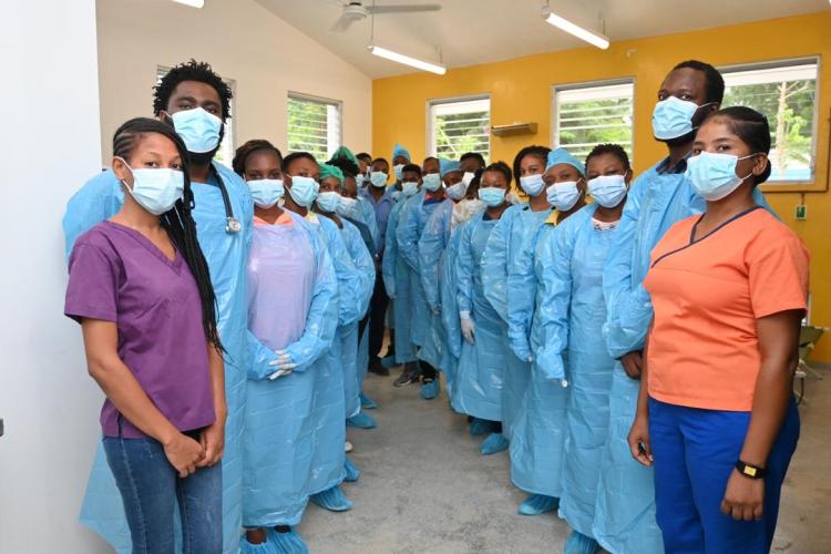 HEI/SBH's cholera response team stand in two rows in a hospital ward. All of the clinicians are wearing blue medical. All but two of the clinicians are wearing light blue protective gowns.