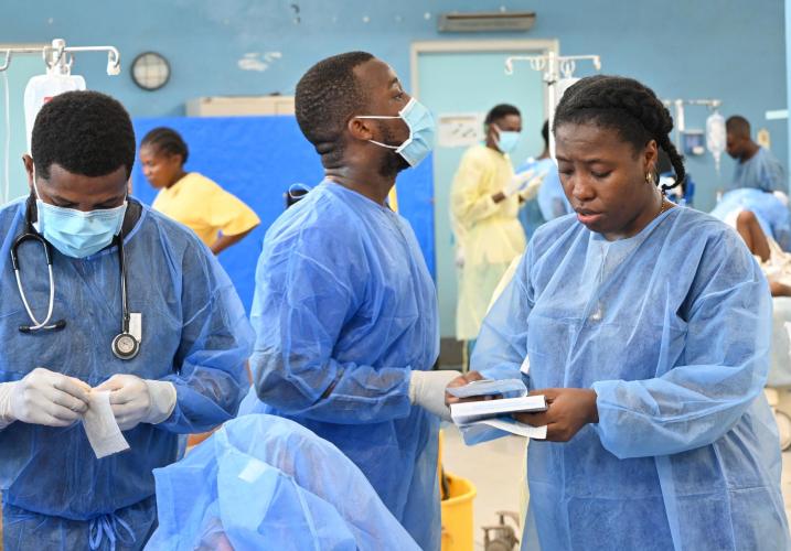 Three Haitian clinicians in blue PPE, in a busy emergency room.