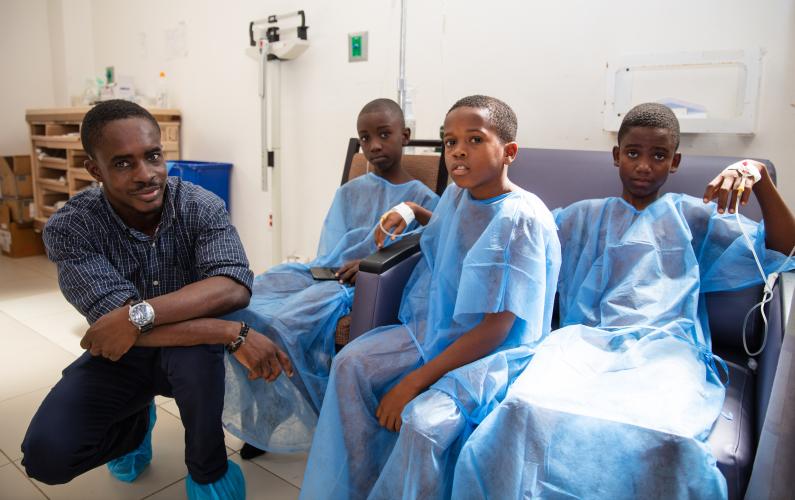 Dr. Jules kneels next to three young haitian boys in hospital gowns in the SBH surgical center.