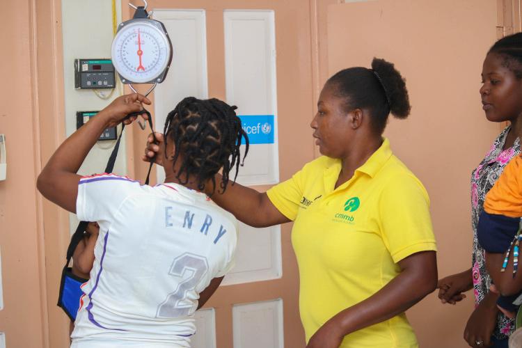 Miss Ginette Elipha, a Haitian community health worker, weighs a young child in the community health room.