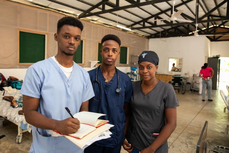 Three Haitian clinicians stand in a row in St. Boniface Hospital's Internal Medicine department. The center and leftmost clinicians are men, the rightmost clinican is a woman.
