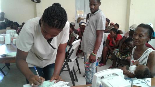 A nurse takes notes as she provides care in a crowded room at a mobile clinic.