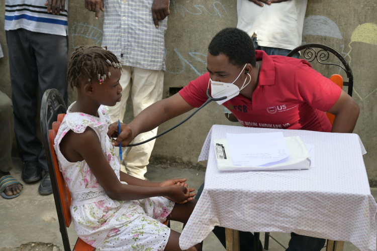 A doctor listens to a young girl's heart using a stethoscope at an earthquake mobile clinic.