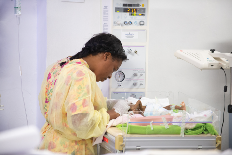 A Haitian woman leans over to examine a baby in a bassinet in St. Boniface Hospital's NICU.