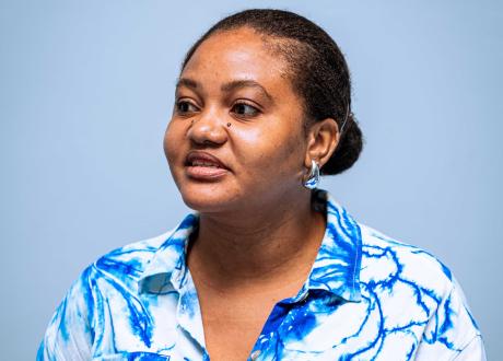 Three-quarters portrait of a Haitian woman in a bright blue and white blouse. Her hair is pulled back into a bun and her lips are slightly parted.
