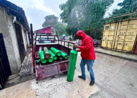 Erick Jolicoeur loads large oxygen bottles into the back of a truck in pouring rain during Hurricane Melissa.