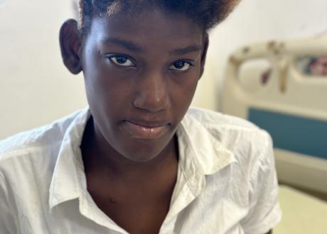 Portrait of a young Haitian woman in a white blouse, looking hesitantly at the camera.