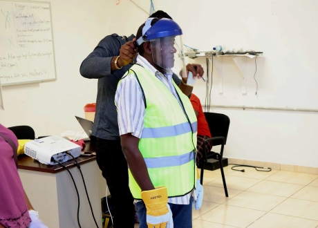 An expert helps a staff member adjust a PPE face shield.