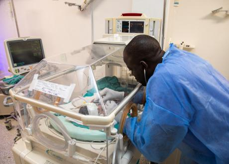 A Haitian clinician uses a stethescope to examin an infant in a NICU incubator