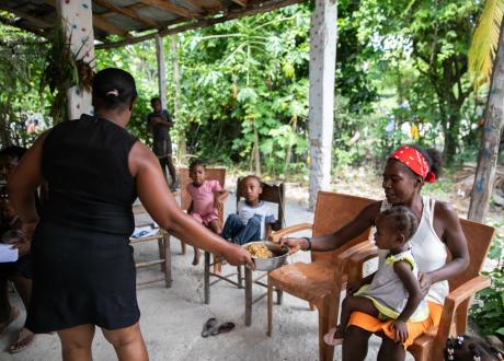 A woman hands a mother and her child a plate of food at at Ti Fwaye session in Lhomond, Haiti.