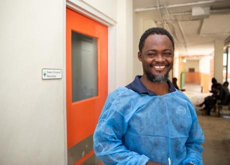 Angelo, a new father, stands outside of St. Boniface Hospital's NICU with a big smile on his face. He is wearing a protective blue medical smock.