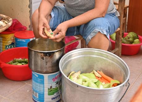 Close shot of a woman’s hands seeding a slice of eggplant next to a large pot with peeled, chopped vegetables.