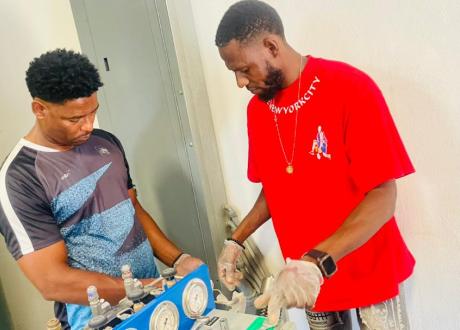 Two Haitian repair technicians work on fixing an oxygen generation system.