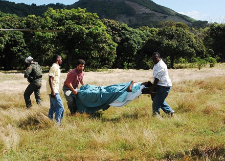 Three men carry a stretcher with a patient on it across a grassy field.