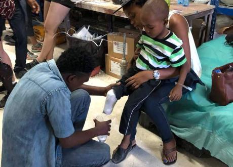 Jamesly's mother holds him in her lap as a prosthetician fits Jamesley with his new prosthetic leg.