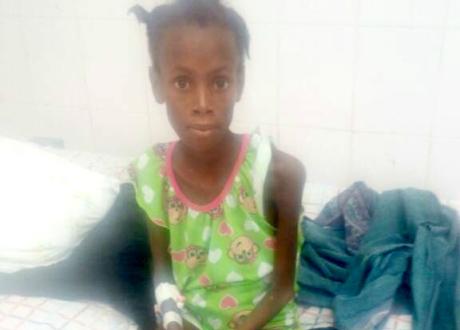 A young Haitian girl sits on a hospital bed with her hands in her lap.
