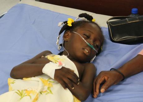 A young Haitian girl wears a nasal cannula while lying on a hospital bed.