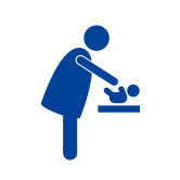 A simple graphic icon of an adult figure leaning over a small table to care for a baby figure. The icon is solid dark blue.