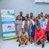 22 Haitian men and women, in business casual attire, pose for a group photo next to a World Pharmacists Day banner, in French, with USAID, MSPP, and HEI logos.