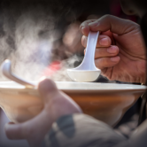 A closeup of a person holding a bowl of soup and lifting a spoonful above the bowl.