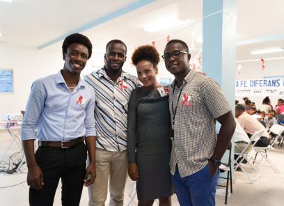Four Haitians in business casual clothes stand together in a large, bright room, smiling and looking relaxed.