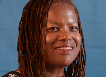 A headshot of Dr. Michele David smiling. She has locs and wears a floral blouse and is situated against a blue background.
