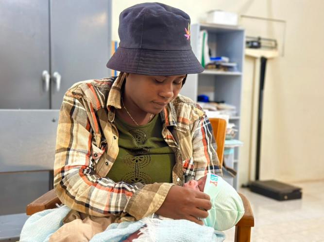 A mother named Chery cradles her newborn baby in her lap, adjusting her baby's cap.