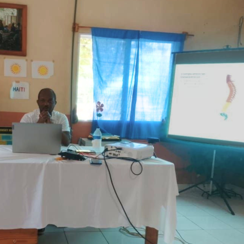 Dr. Bertony Guerrier sits behind a table as he lectures about maternal health and spinal cord injuries.