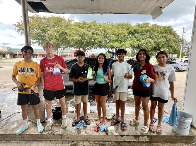 A group of high school students pose with car washing tools and equipment at their fundraiser.