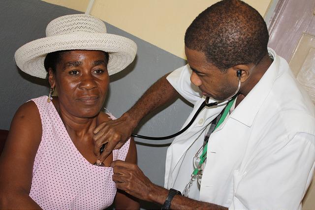 Male doctor in white coat using a stethoscope to listen to a woman's heart.