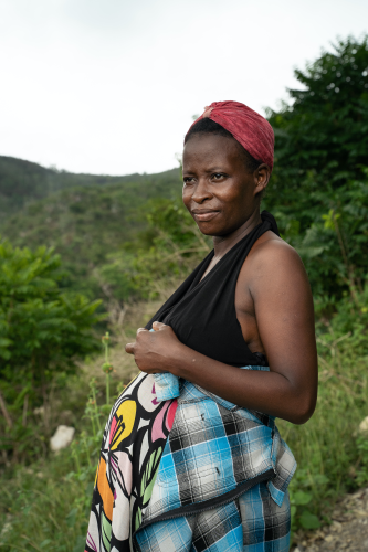 A Haitian woman stands in profile with her hands on top of her pregnant belly. She smiles and looks off into the distance.
