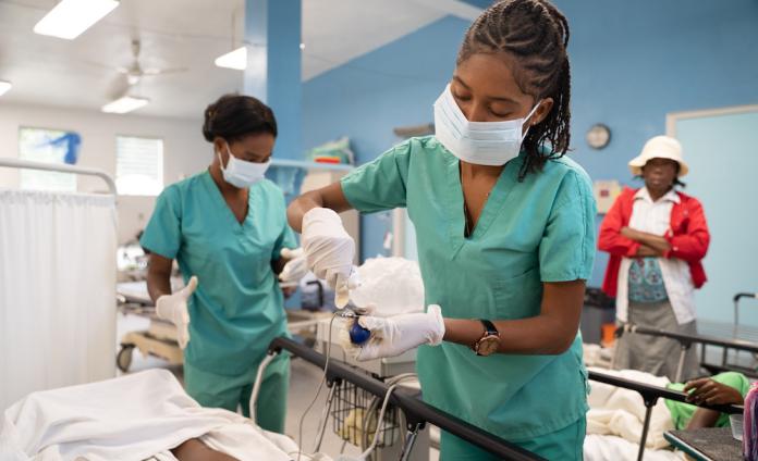 Two young women Haitian nurses tend to a patient in a hospital bed in the emergency room.