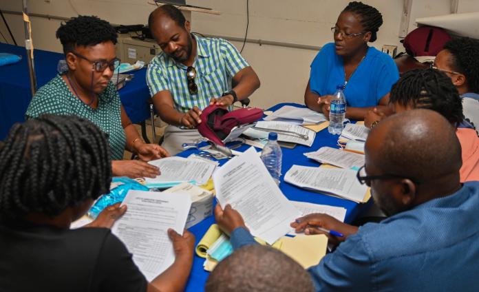 A group of Haitian clinicians are gathered around a table filled with papers and medical equipment.