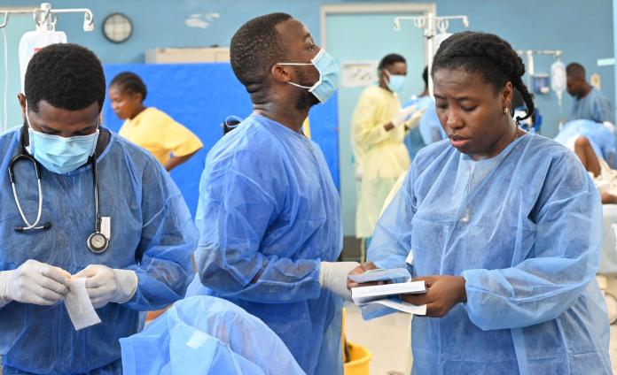 Three Haitian clinicians in blue PPE, in a busy emergency room.