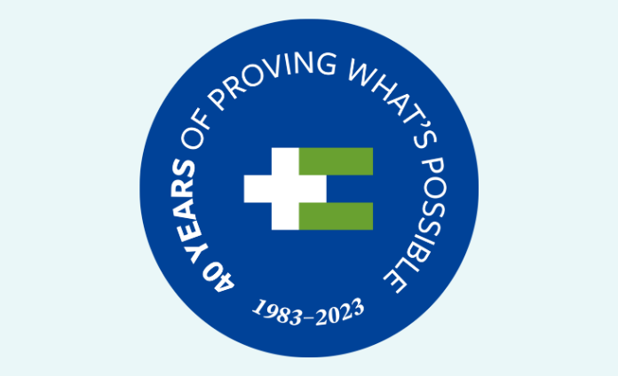 The HEI/SBH 40th anniversary logo on a light blue background. The logo is a round dark blue logo with a white plus sign and green equal sign in the middle. Around the plus-equal symbol it says "40 years of proving what's possible 1983-2023"