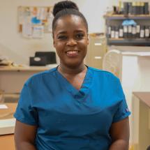 Smiling Haitian woman with hair in a bun, wearing blue scrubs