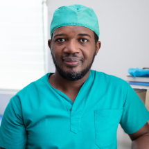 A headshot of Dr. Berthony Guerrier wearing teal scrubs and a matching surgical cap.