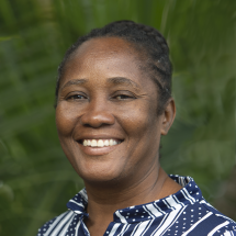 A headshot of Dr. Miliane Clermont smiling while wearing a striped and polka-doted dark blue collard shirt against a green background.