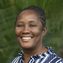 A headshot of Dr. Miliane Clermont smiling while wearing a striped and polka-doted dark blue collard shirt against a green background. 