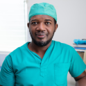 A headshot of Dr. Berthony Guerrier wearing teal scrubs and a matching surgical cap.