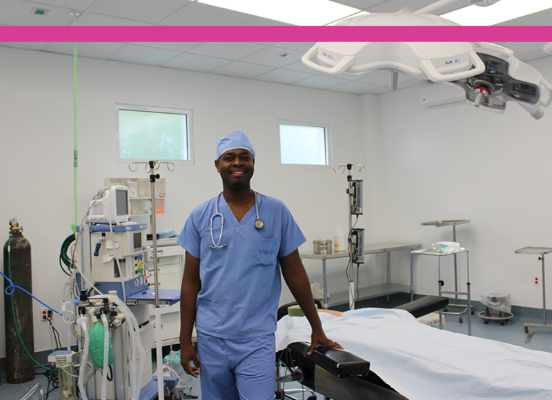 A photo of a surgical suite with a Haitian surgeon standing in the middle of the room and smiling. He is surrounded by equipment.