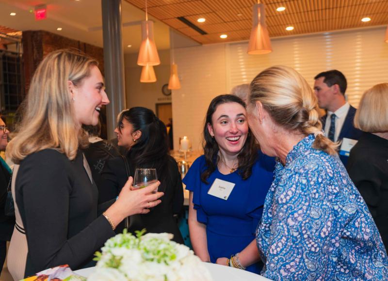 A half-dozen formally-dressed adults in laughter and conversation, in a large, warmly-lit room.