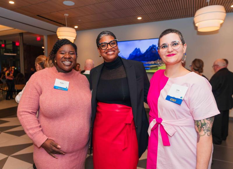 Three women, two Black and one white, pose together, smiling happily. 