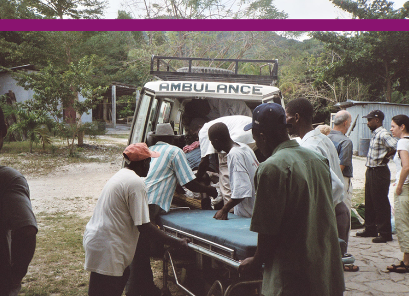 An old photo of a SBH ambulance, with Haitian health professionals helping a patient out of the back of the vehicle.